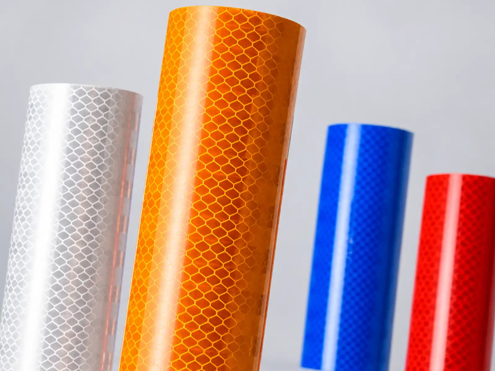 Rollos de lámina microprismática en blanco, naranja, azul y rojo, con el patrón de panal a la vista