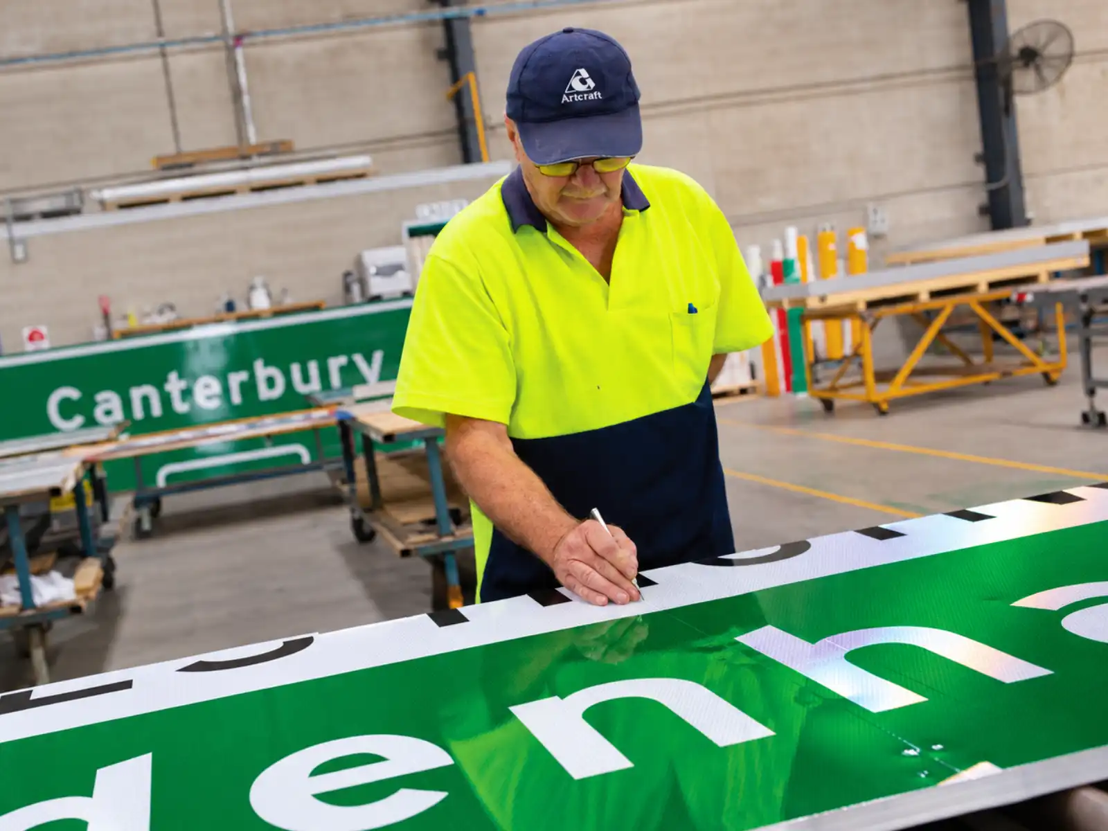 Operario trabajando una señal verde con letras blancas en un taller