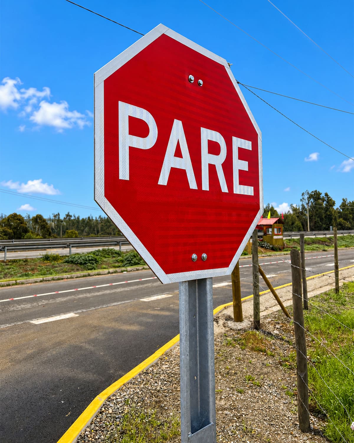 Señal de PARE reflectante junto a una carretera, con una caseta y un cerco perimetral de fondo