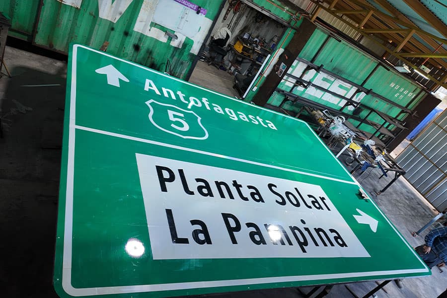 Letrero vial verde "Antofagasta" recién fabricado sobre una mesa de trabajo, con el interior del taller de fondo